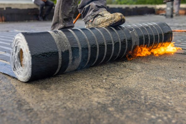 Workers placing a vapor barrier on the roof using a propane gas torch for welding bitumen sheets